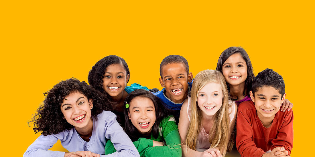 Group of kids lay bunched up on the ground smiling and laughing against yellow backdrop